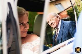 At The Italian Villa in Dorset, UK, the bride prepares to exit her car before the ceremony, while her father’s reflection appears in the door’s glass, capturing a poignant and anticipatory connection before she enters the venue.